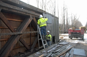 The interior siding was removed from the north side of the historic 1918 Snyder Brook rail bridge, revealing diagonal wood trusses and vertical bolts secured by (unseen) large nuts, on Tuesday, Dec. 2, as part of the preparations for Friday’s lift by brothers Harlan and Vernon Crawford of Canaan, Vt., both crew members of Northern New England Field Services, LLC, of Stewartstown, owned by Dennis Thompson who provided on-site direction throughout the project.